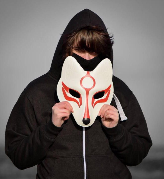 Kit Kanthan with his mask on stood in front of a bookshelf.